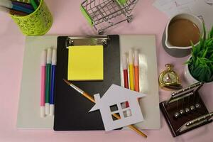 Top view of the cutting paper or drawing house on a pink table, preparing to do homework in a clipboard. Drawing Working Desk Concept photo