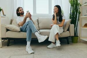 A man looks at his phone screen and smiles during an argument with his girlfriend. The angry and hurt woman looks in his direction and is sad. Family discord at home, phone addiction photo