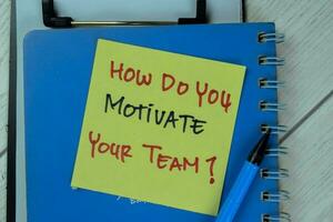 Concept of How Do You Motivate Your Team write on sticky notes isolated on Wooden Table. photo