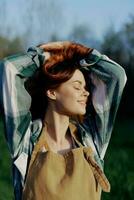 retrato de un mujer con un hermosa sonrisa en su trabajo ropa y delantal en naturaleza, disfrutando relajación después trabajo en el puesta de sol luz de sol foto