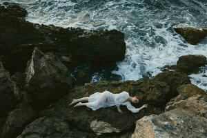 beautiful young woman in long white dress wet hair lying on a rocky cliff landscape photo