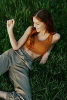 Happy redheaded woman sitting on fresh spring green grass in the garden smiling and looking out into the sun, view from above, harmony with nature photo