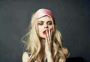 blonde woman smeared makeup on her face on a gray background and a pink sleep mask on her head photo