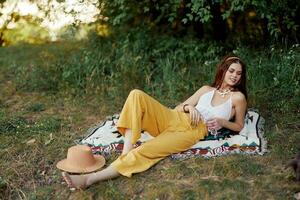 Young beautiful hippie woman lying on the ground in nature in the fall in eco clothes in yellow pants in the sunset light photo