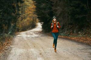energetic woman running along the road with backpack in autumn forest photo