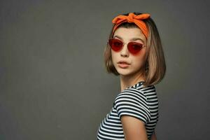 mujer en Gafas de sol con un naranja vendaje en su cabeza en un a rayas camiseta Moda foto