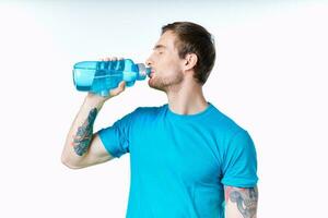 sexy athletes with a bottle of water and in a blue t-shirt on a white background drink photo