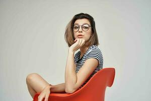 pretty woman with glasses sitting on the red chair light background Lifestyle photo