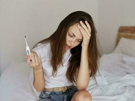 upset woman with a thermometer in her hands sitting on the bed health problems photo