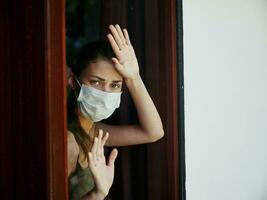 woman in medical mask holds hands on window ban lockdown photo