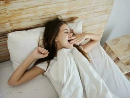 woman yawns lying in bed after morning sleep photo