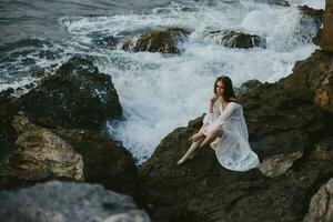 barefoot woman in white dress sits on a stone with wet hair unaltered photo