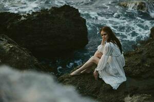 A woman in a white wedding dress is sitting barefoot on a wave cliff photo