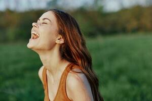 A young woman laughing and smiling merrily in nature in the park with the sunset lighting illuminating her long red hair photo