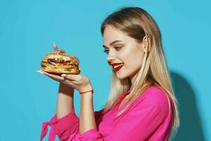 alegre rubia en un rosado camisa hamburguesa rápido comida bocadillo azul antecedentes foto