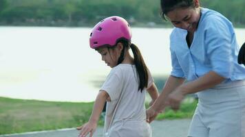 madre enseñando su hija cómo a patineta en el parque. niño montando patinar tablero. sano Deportes y al aire libre ocupaciones para colegio niños en el verano. video