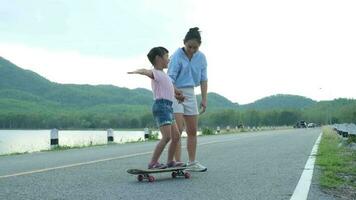 madre insegnamento sua figlia Come per skateboard nel il parco. bambino equitazione pattinare tavola. salutare gli sport e all'aperto attività per scuola bambini nel il estate. video
