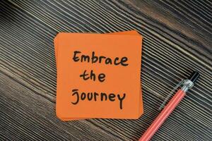 Concept of embrace the journey write on sticky notes isolated on Wooden Table. photo