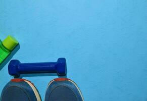 blue dumbbell and sneakers indicating workout plan on blue background. Top view with copy space for any design. Healthy and fitness concept photo