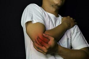 Asian Man Holding his hand. He feels pain on his elbow with black background. Medical or healthcare concept photo