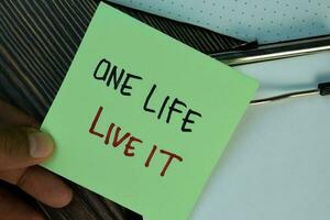 One Life Live It write on sticky notes isolated on Wooden Table. photo