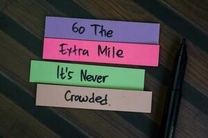 Go The Extra Mile It is Never Crowded write on sticky notes isolated on Wooden Table. photo