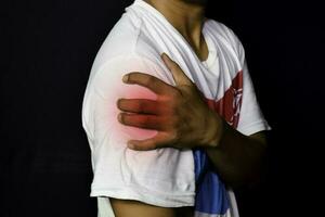 Asian Man Holding his hand. He feels pain on his shoulder and upper arm with black background. Medical or healthcare concept photo