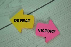 Defeat or Victory write on sticky notes isolated on Wooden Table. photo