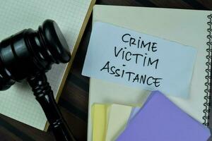 Concept of Crime Victim Assistance write on sticky notes with gavel isolated on Wooden Table. photo