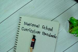 Concept of National School Curriculum Standards write on a book isolated on Wooden Table. photo