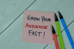 Concept of Grow Your Audience Fast write on sticky notes isolated on Wooden Table. photo