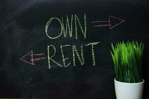 Own or Rent written with color chalk concept on the blackboard photo