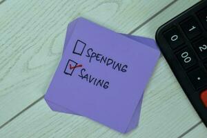 Concept of Spending or Saving Saving write on sticky notes isolated on Wooden Table. photo