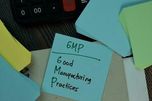 GMP - Good Manufacturing Practices write on sticky notes isolated on Wooden Table. photo