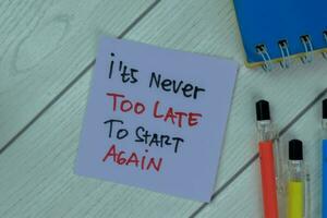 Concept of It's Never Too Late To Start Again write on sticky notes isolated on Wooden Table. photo