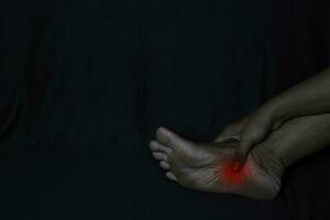 Asian Man Holding his foot. He feels pain foot heel with black background. Plantar Fascilitis. Medical or healthcare concept photo