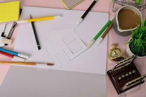 Top view of the cutting paper or drawing house on a pink table, preparing to do homework in an open notebook. Drawing Working Desk Concept. photo