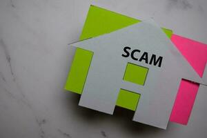 Property Scam write on sticky note and house made from paper isolated on Office Desk. photo