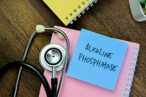 Concept of Alkaline Phosphatase write on sticky notes with stethoscope isolated on Wooden Table. photo