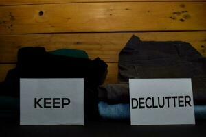 Keep and Declutter write on a sticky note between fashion clothes folded and stack isolated on wooden background. photo