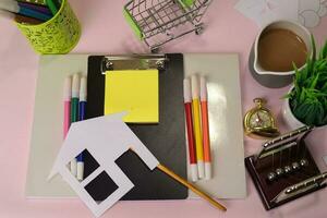 Top view of the cutting paper or drawing house on a pink table, preparing to do homework in a clipboard. Drawing Working Desk Concept photo