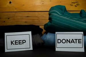 Keep and Donate write on a sticky note between fashion clothes folded and stack isolated on wooden background. photo