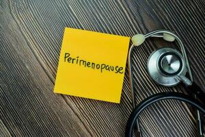 Concept of Perimenopause write on sticky notes with stethoscope isolated on Wooden Table. photo