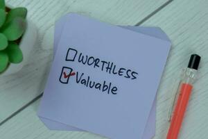 Concept of Worthless or Valuable Valuable write on sticky notes isolated on Wooden Table. photo