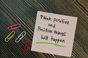 Think positive and positive things will happen write on sticky notes isolated on Wooden Table. Motivation concept photo