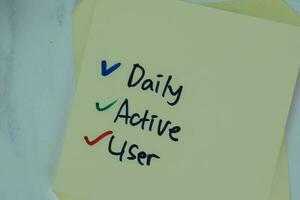 Daily Active User write on sticky notes isolated on Wooden Table. photo