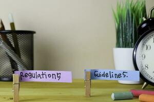 Regulations and Guidelines. Handwriting on sticky notes in clothes pegs on wooden office desk photo
