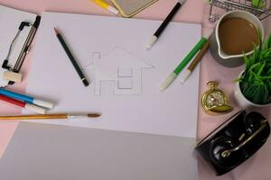 Top view of the cutting paper or drawing house on a pink table, preparing to do homework in an open notebook. Drawing Working Desk Concept. photo