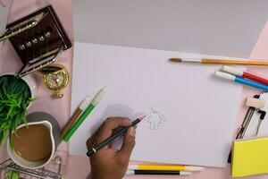 parte superior ver de el del hombre manos dibujo en un rosado mesa, preparando a hacer deberes en un abierto cuaderno con un marcador en mano. dibujo trabajando escritorio concepto. foto