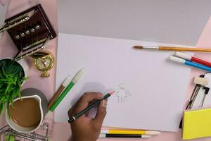 Top view of the man's hands drawing on a pink table, preparing to do homework in an open notebook with a marker in hand. Drawing Working Desk Concept. photo